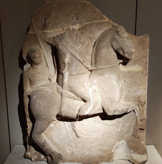 A stele depicting a horseman carrying a shield, followed by a young man with two spears, dating to the 3rd century BCE