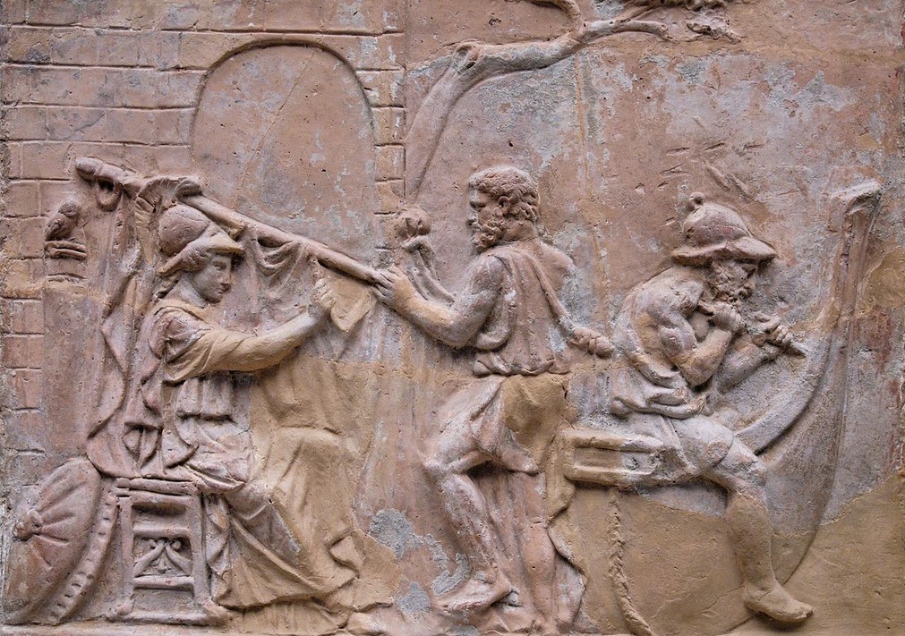 The building of the ship Argo: Athena (on the left) adjusts the sail; Tiphys (centre) holds the yard; Argos (on the right) sits across the stern. Terracotta relief, Roman artwork, probably 1st century CE. Said to have been found near the Porta Latina in Rome