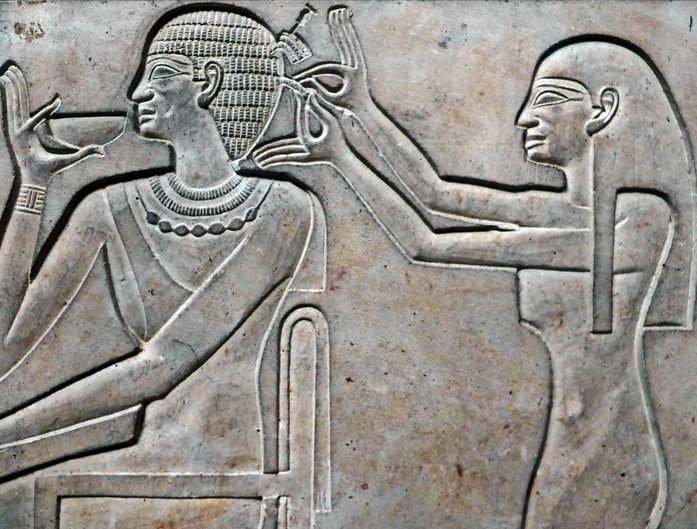 Detail of the Sarcophagus of Queen Kawit, Wife of MENTUHOTEP II.- Egyptian Museum Cairo. The queen is depicted with short hair, she is sitting on a chair, a servant girl is arranging her hair, while a servant is pouring her a drink.